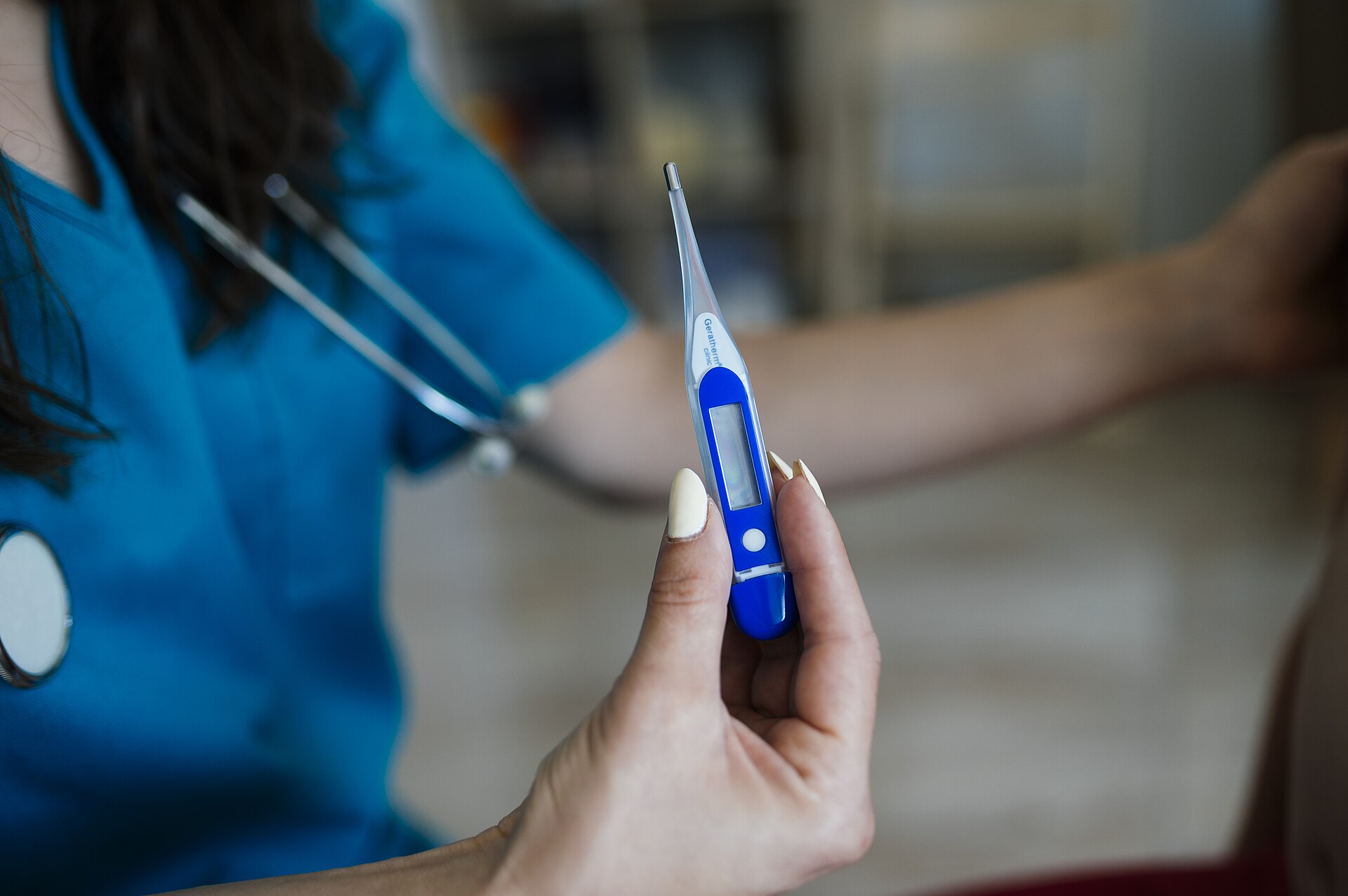 A clinician in scrubs holding a digital thermometer during a visit