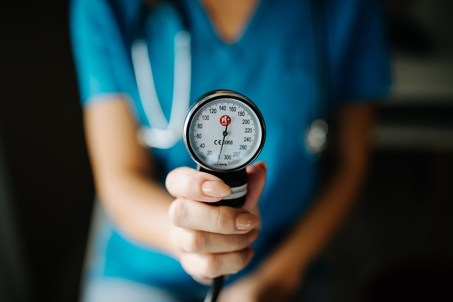 A clinician holding out an aneroid blood pressure gauge toward the camera
