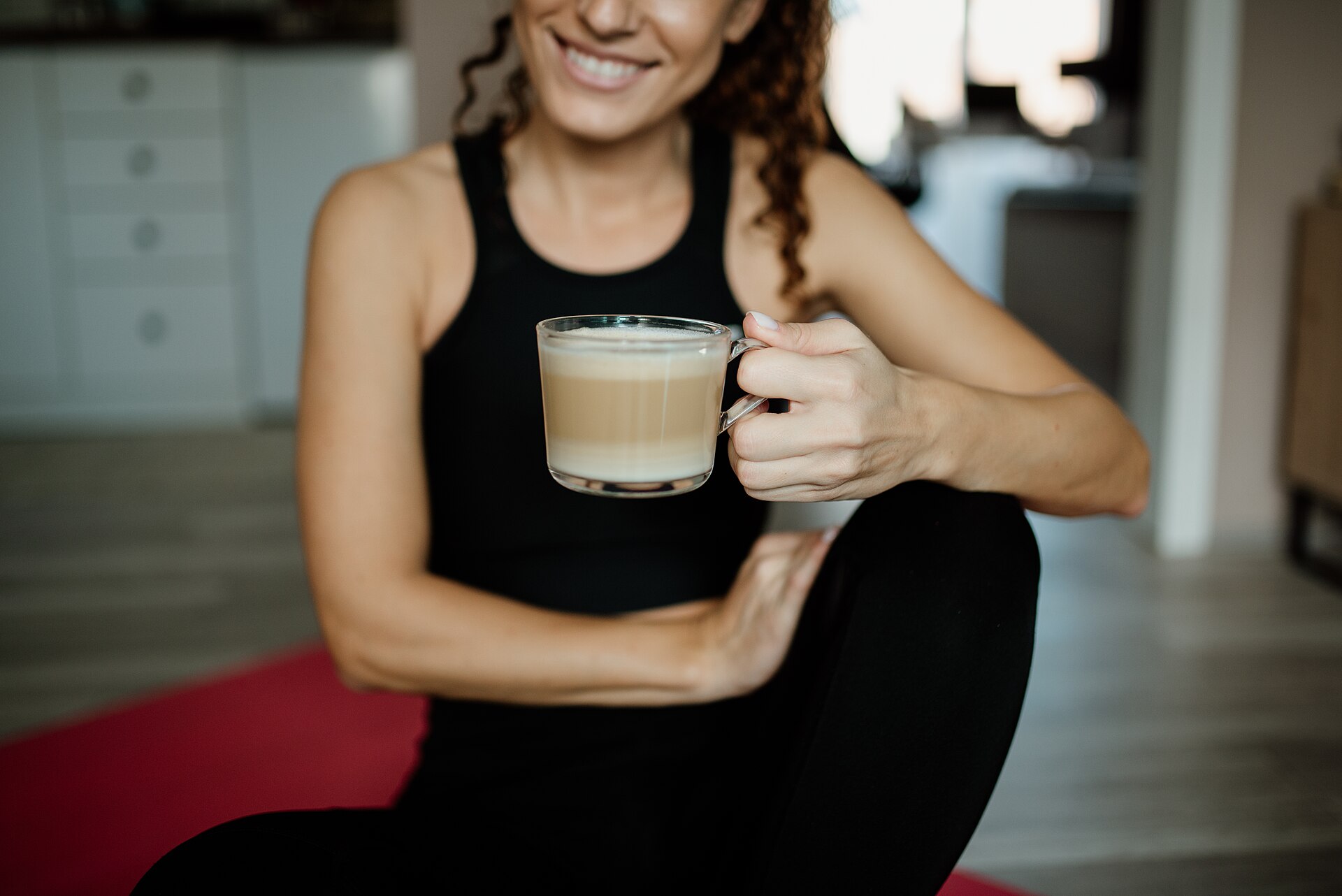 A woman in activewear resting on a yoga mat holding a warm drink